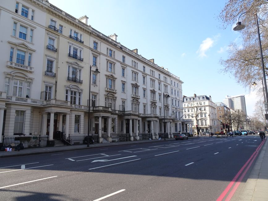 A wide-angle view of a residential street in South Kensington with elegant white Victorian-style buildings featuring decorative cornices, tall windows, and balconies. The street is lined with leafless